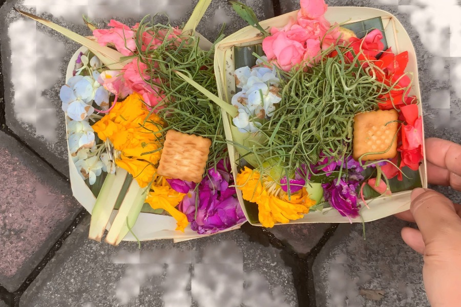 Two Canang Sari offerings placed on gray pavement