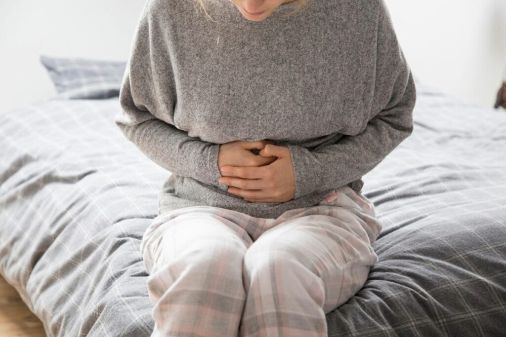 Traveler sitting on a bed holding their stomach, showing discomfort linked to Bali Belly illness.