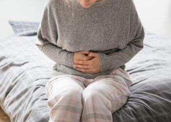 Traveler sitting on a bed holding their stomach, showing discomfort linked to Bali Belly illness.