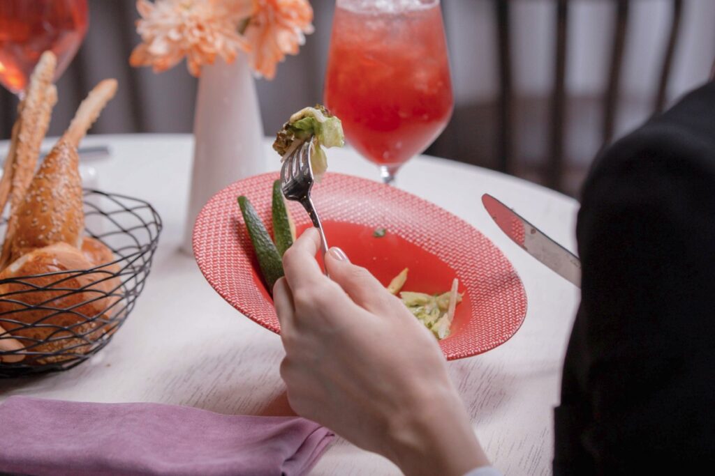 Person eating a plated dish with vegetables and drink at a fine dining restaurant in Bali.