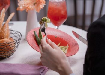 Person eating a plated dish with vegetables and drink at a fine dining restaurant in Bali.