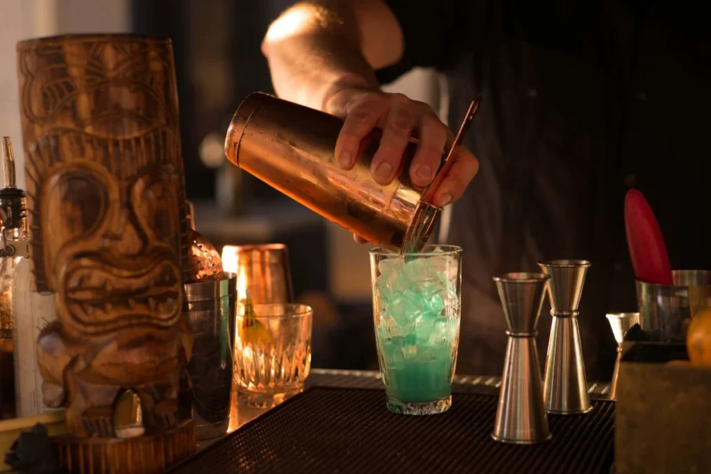 Bartender pours blue cocktail into glass with ice, showing tropical mixology at Bali cocktail bars.