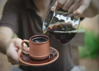 Person pours fresh black coffee into clay cup, showing Bali specialty coffee culture from Kintamani to Canggu.