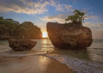 Sunset view at Padang Padang Beach with large seaside rocks and gentle waves on the shore.