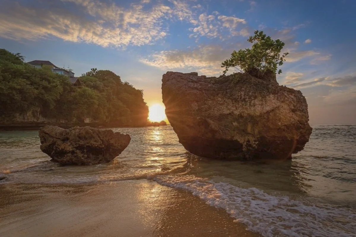 Sunset view at Padang Padang Beach with large seaside rocks and gentle waves on the shore.