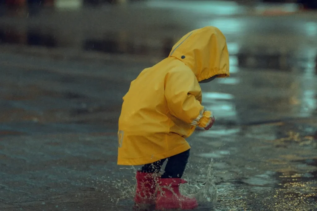 Child wearing raincoat and boots playing outside during rainy day in Bali.