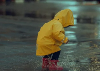 Child wearing raincoat and boots playing outside during rainy day in Bali.