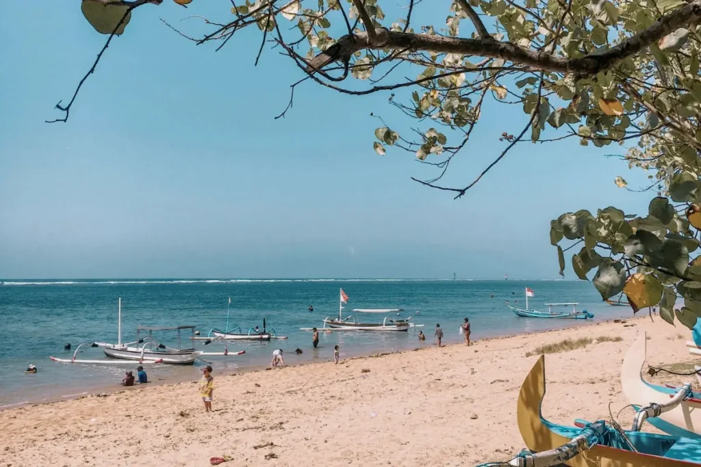 People relax on Sanur Beach with traditional boats, showing one of the best places to enjoy Bali's east coast.