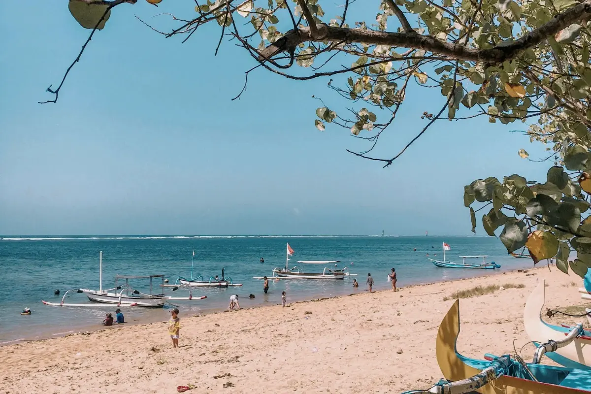 People relax on Sanur Beach with traditional boats, showing one of the best places to enjoy Bali's east coast.