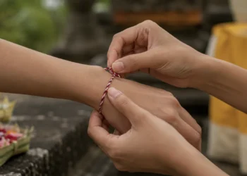 Hands tie a Tridatu bracelet on a wrist during a Balinese blessing ceremony, symbolizing spiritual protection and balance.