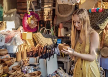 Traveler examines a wooden bowl among handmade bags, baskets, and souvenirs at Ubud Art Market.