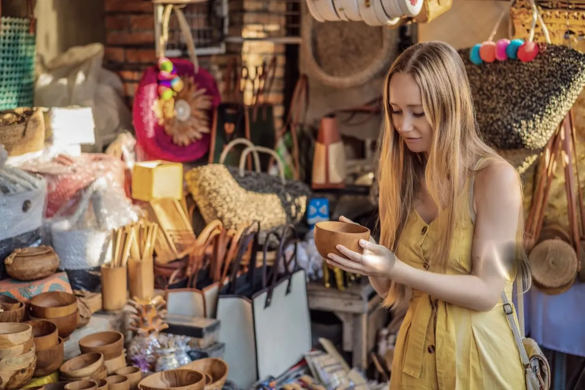 Traveler examines a wooden bowl among handmade bags, baskets, and souvenirs at Ubud Art Market.