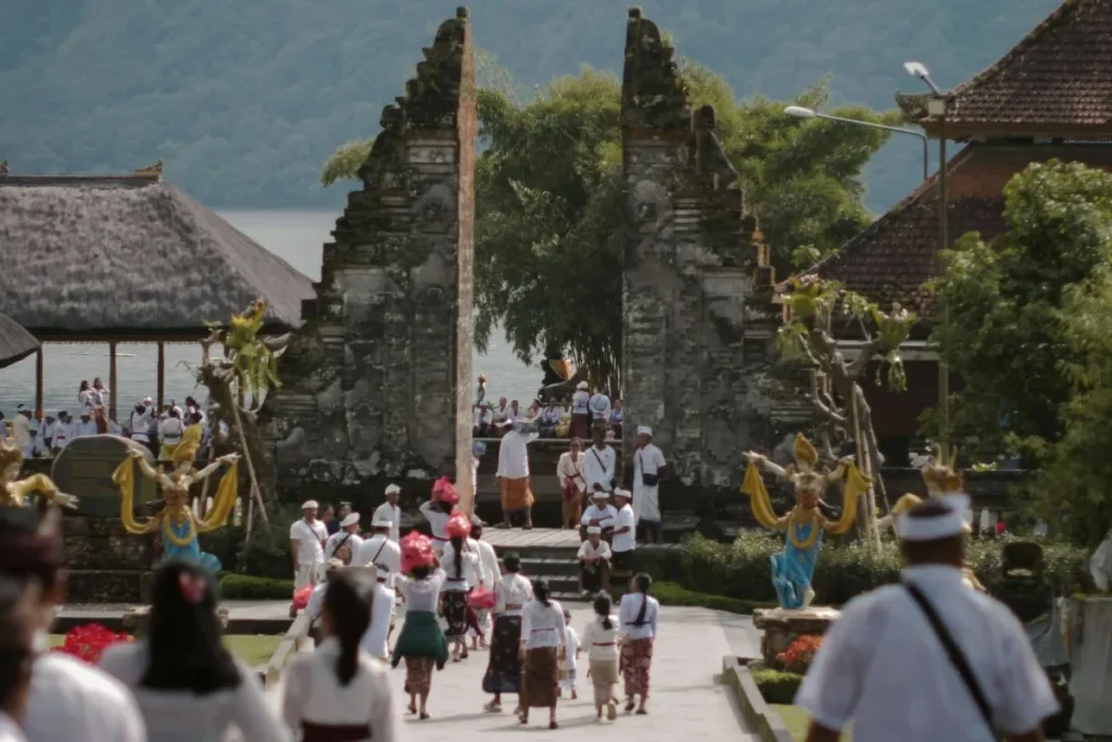 Visitors wearing traditional temple clothing walk toward a Balinese temple entrance during a religious ceremony.