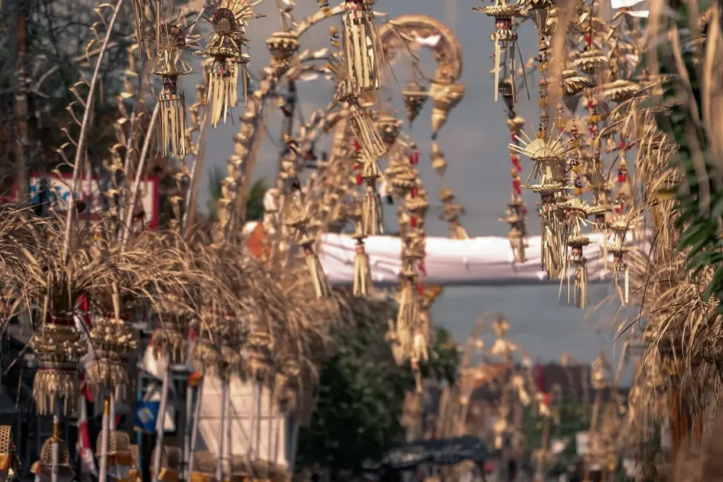 Rows of decorated Balinese penjor line a street during Galungan, with traditional offerings and decorations visible.