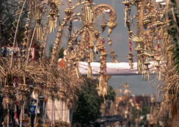 Rows of decorated Balinese penjor line a street during Galungan, with traditional offerings and decorations visible.