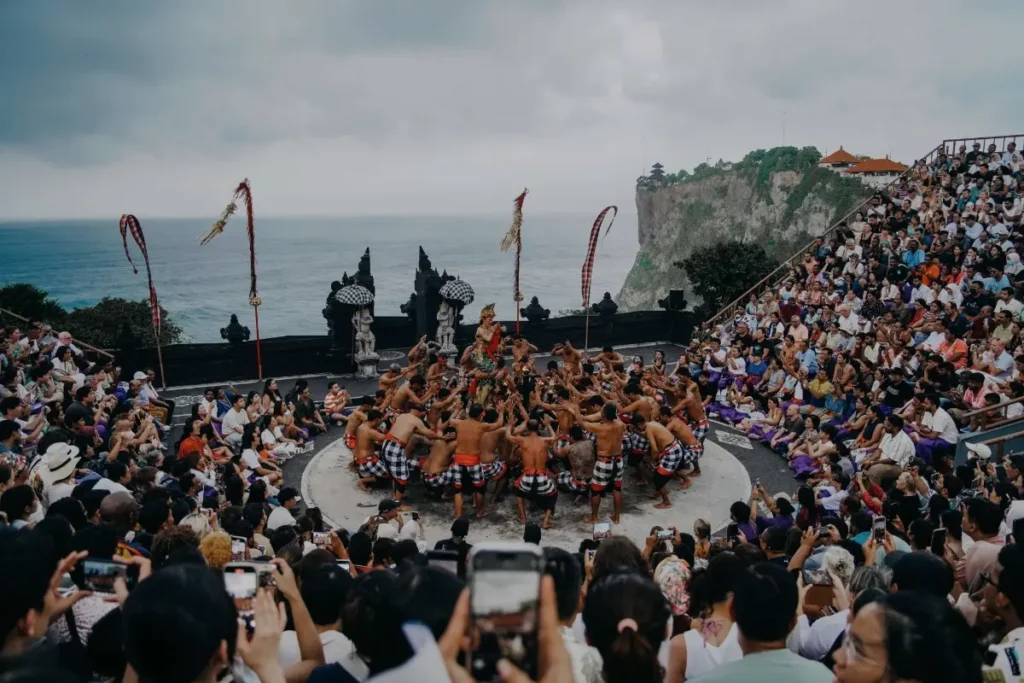 Performers perform the Kecak dance at Uluwatu Temple, surrounded by a large audience overlooking the ocean.