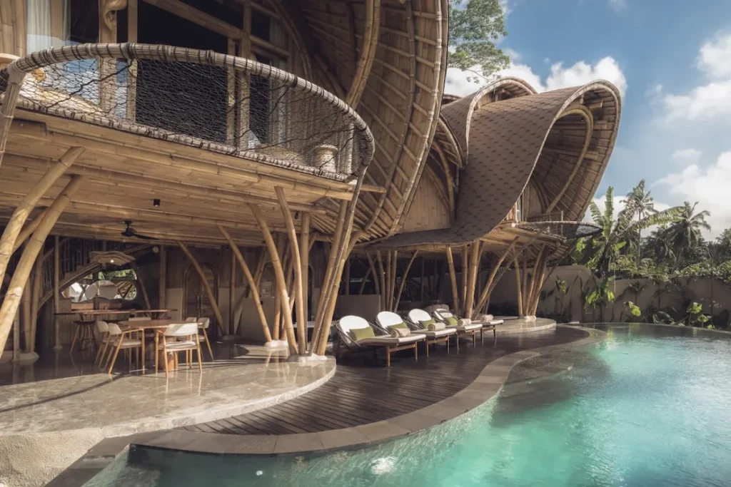 Bamboo eco resort with curved architecture, poolside loungers, and tropical greenery surrounding the sustainable Bali stay.