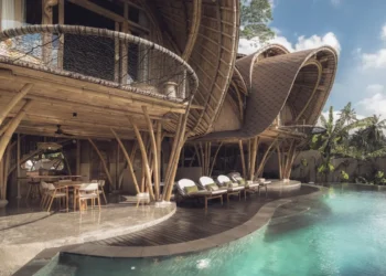 Bamboo eco resort with curved architecture, poolside loungers, and tropical greenery surrounding the sustainable Bali stay.