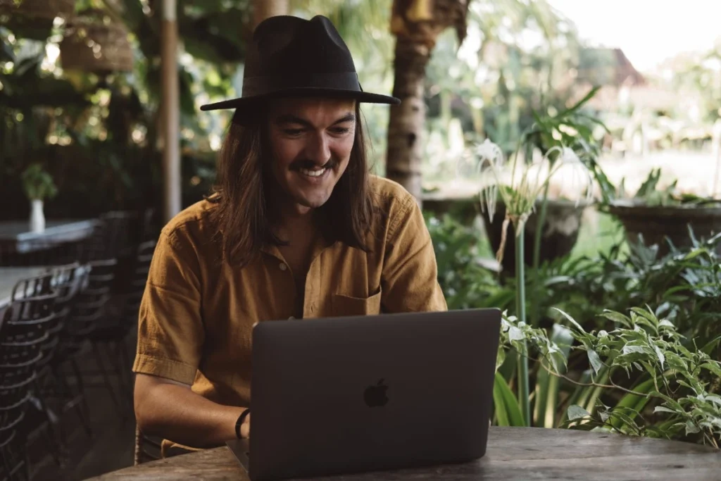 A digital nomad works on a laptop at an outdoor table surrounded by tropical greenery in Bali.