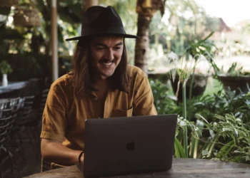 A digital nomad works on a laptop at an outdoor table surrounded by tropical greenery in Bali.
