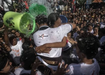 Participants celebrate Omed-Omedan as a crowded water ritual, with people pouring water over young participants in Denpasar.